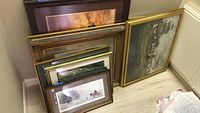 Photo showing several horse-themed framed prints stacked and leaning against a wall, showcasing various sizes and frames.