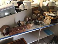 Wide view of shelf with three large sea shells, various decorative items like incense boxes, bookends, picture frames, and a box of records in the background.