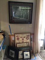Overall view of ten framed artworks leaning against a wall including a large tree-lined walkway print and smaller pieces