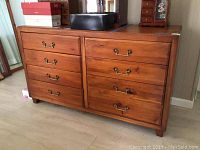 Front view of wooden dresser showing eight drawers with brass handles and surface partially occupied with items.