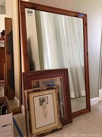 Wood framed mirror leaning against wall with three framed nude art prints resting against it