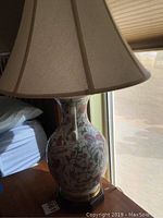 Side view of one ceramic lamp showing floral pattern on body and beige fabric lampshade.