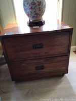 Front view of a wooden nightstand with two drawers and metal handles, showing some surface scratches.