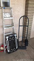 Wide view showing 5 foot aluminum step ladder, black plastic folding dolly, and black metal flat cart with handle