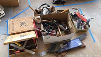 Wide view of assorted hand tools including saws, drills, screwdrivers in boxes and tool bags.