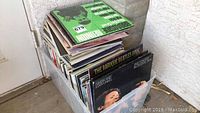 Stack of vintage vinyl records in a plastic storage bin, showing various album covers at the top