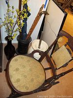 Full view of vintage wooden rocking chair with floral fabric cushions, black metal umbrella stand, dark glass vase with artificial yellow flowers, walking stick and cane, and blue umbrella.