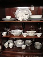 Photo of Noritake Macis china pieces arranged on shelves including plates, bowls, cups, saucers, and assorted stemware glasses.