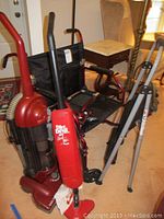 The lot showing a Dirt Devil Stick Vac Plus vacuum, folding Medline wheelchair with black fabric seat and red frame, Cosco gray step ladder and part of the Eureka Maxima vacuum.