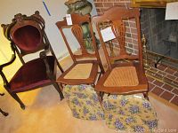 Three vintage chairs arranged next to a fireplace, showing the two cane seat chairs and the larger upholstered armchair with carved wood frames.