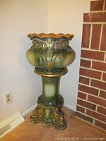 Full view of green and gold ornate jardiniere on matching pedestal against wall