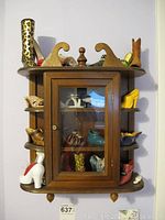 Front view of wooden wall cabinet filled with various miniature shoe figurines on shelves and inside cabinet.