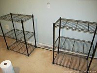 Two black metal wire shelving units side by side against a wall.