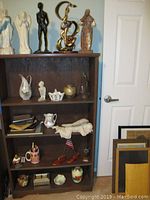 Wooden shelf with various figurines, glass and ceramic decorative items, a sleeping angel statue, books, and a plastic bottle near the bottom right.