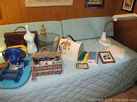 Overall view of the lot items on a blue quilted surface including OttLite desk lamp, sewing boxes, briefcase, desk fan, sports radio, hand weights, wooden figurine, trash can, and others for identification and condition assessment.