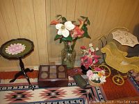 View of the entire grouping of items from left to right: wood side table, photo box, tall glass vase with faux flowers, small floral figurines, small baskets, and yellow doll carriage.