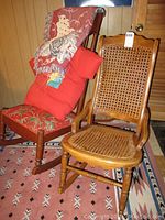 Two wooden rocking chairs side by side on a patterned rug, one with cane seat/back and one with patterned fabric seat, with pillow and throw blanket on the fabric chair.