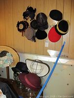 Wood wall mounted hats and racks with various vintage hats hung on wall with glass display heads below.