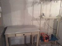 Vintage wood table with white enamel top with visible chips, single drawer, and wooden legs shown against wall