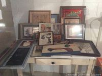 Wide view of all vintage framed items arranged on and behind a table, showing variety of art, signs, chalkboards, and photographs.