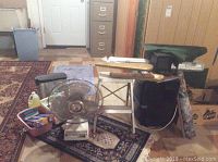 Wide view of lot contents including fan, small heater, step stool, wall hangings, trash can, and cleaning supplies.