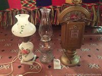 Front view of three lamps: white floral kerosene lamp with chip on shade on marble base, clear glass hurricane kerosene lamp, and heavy Chicago parking meter lamp