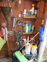 Shows assorted garden and household chemicals on shelves, hanging metal planter, hand tools, and green garden stool.