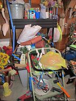 Image showing the lot contents including green folding metal step ladder, several holiday-themed door mats with floral and welcome designs, mallet, gardening items, and household supplies.
