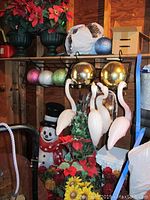 Photo showing two pink plastic flamingos, plastic snowman figure, red poinsettias, assorted faux flowers, and large gold spherical ornaments.
