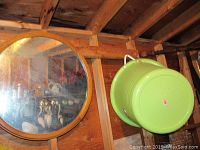 Round wooden framed wall mirror hanging on wooden wall with reflection of room visible in glass.
