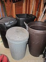 Four trash cans grouped: one metal with cracked lid, three plastic (black, brown, and rectangular black)