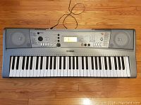 Top view of Yamaha Portatone YPT-310 electronic keyboard showing 61 keys and speakers at both ends with power cord attached.