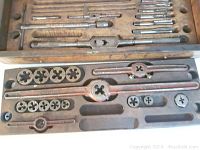 Top view of open vintage wooden tool and die box showing multiple metal threading dies, tap wrench handles, and threading taps neatly organized in cutouts.