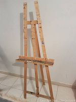 Front angled view of the wooden artist easel showing adjustable center support and paint marks on wood.
