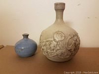 Two mid-century modern vases side by side, larger cream-colored vase with floral relief decoration and smaller blue vase.