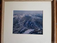 Framed aerial vintage photograph of snowy mountain ski resort with undefined signature in bottom right corner.