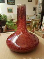 Full view of vase showing bulbous base and long neck with sang de boeuf red glaze transitioning to white at the lip.