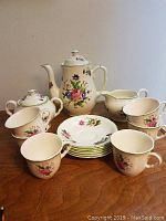 Full set of Midwinter vintage English porcelain floral coffee set including coffee pot, four cups, four saucers, creamer, and sugar bowl arranged on wooden surface.
