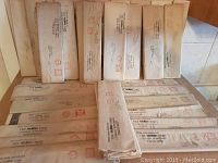 Photo showing a stack of unopened vintage British newspapers and periodicals in original mailing envelopes, arranged in two rows.