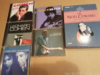Photo of six items: three Leonard Cohen CDs, one Bob Dylan CD, one Eric Clapton CD, and one Noel Coward DVD box set.