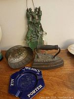Overview of all vintage collectible items on wooden surface including the ashtray, milk bottle, flat iron, cast iron plaque, and metal mould