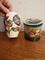 View of both vase and lidded cylindrical box showing floral designs and size comparison