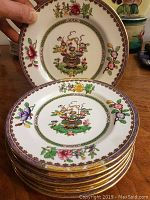 Stack of 6 cake plates with floral basket design and gold trim held to show pattern details