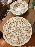 Photo showing stacked dinner plates and soup bowls with detailed floral design and scalloped edges.
