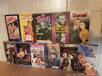 Full view of 11 VHS tapes arranged in two rows showing cover art, titles, and condition.