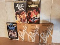 Photo showing six VHS tapes of classic Humphrey Bogart films arranged on a surface with visible titles and cover art.