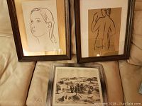 Three framed lithograph reproduction prints laid on a bed, two vertical line drawings of female figures and one landscape horizontal print.