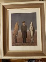 Framed print featuring a man in suit and bowler hat standing between a large bird and fish in a barren landscape.