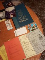 Photo of 1981 World Atlas book, postcards, printed world recipes sheets with decorative vintage illustrations, and other paper items.