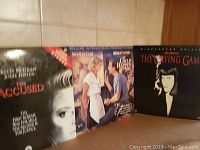 Three vintage LaserDiscs in their original cases, standing upright against a tiled wall.